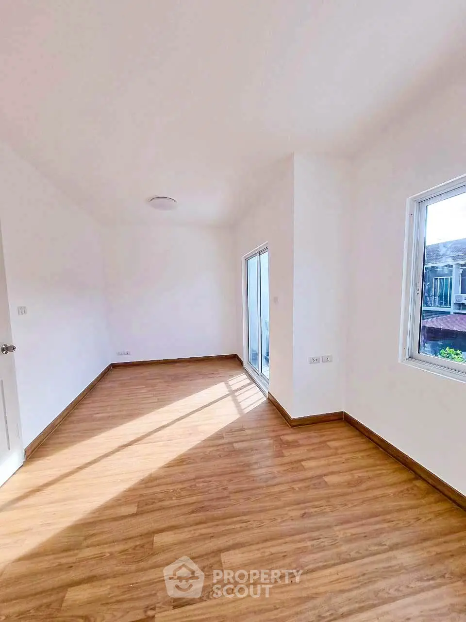Spacious sunlit room with wooden flooring and large windows in modern home.