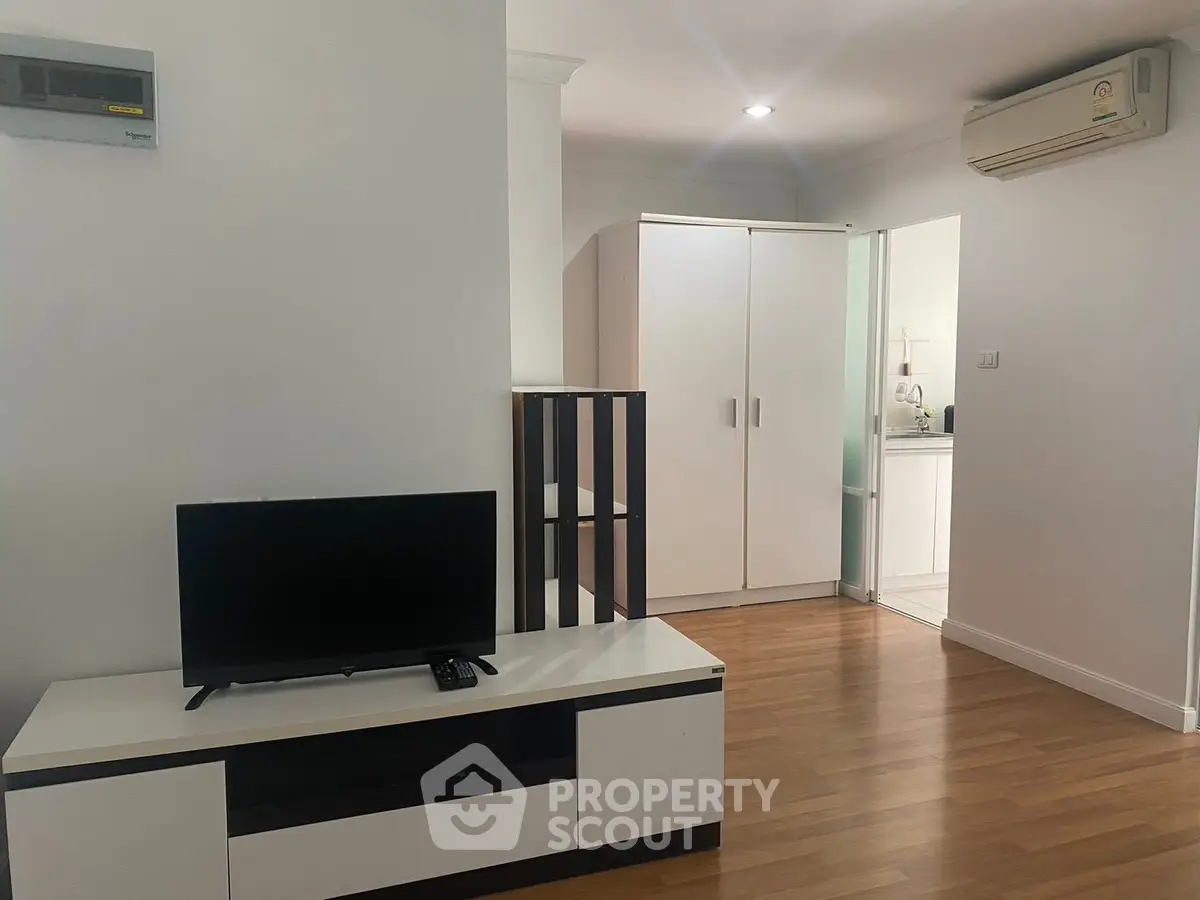 Modern living room with sleek furniture and wooden flooring, featuring a TV and air conditioning.