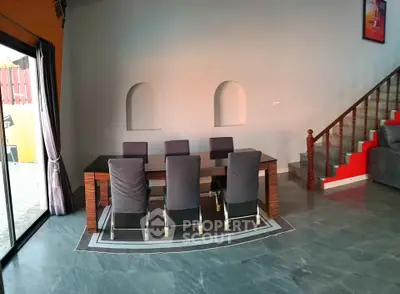 Modern dining area with sleek table and chairs, adjacent to stylish staircase in open-plan living space.