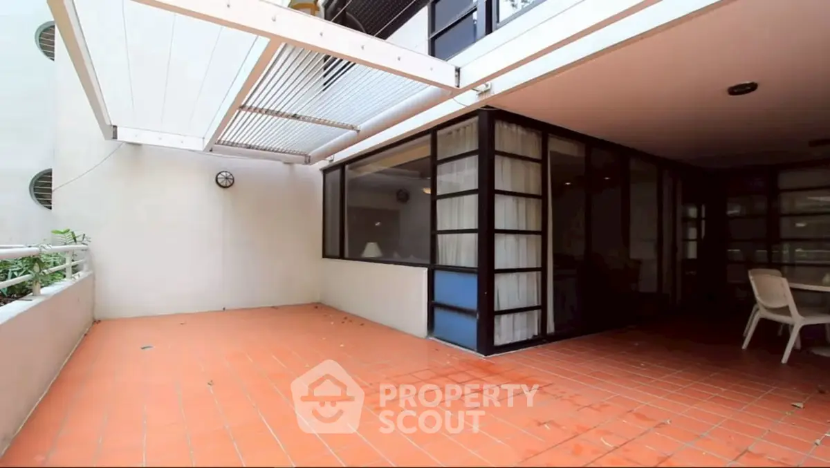 Spacious balcony with terracotta tiles and modern glass doors in urban apartment.