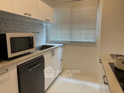 Modern kitchen with sleek white cabinets, dishwasher, and microwave, featuring a stylish hexagonal backsplash.