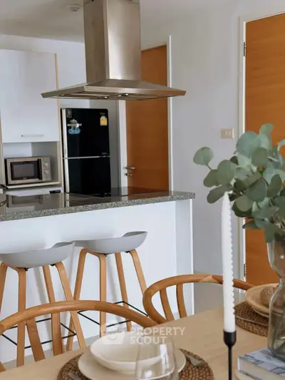 Modern kitchen with island, bar stools, and dining setup in stylish apartment.