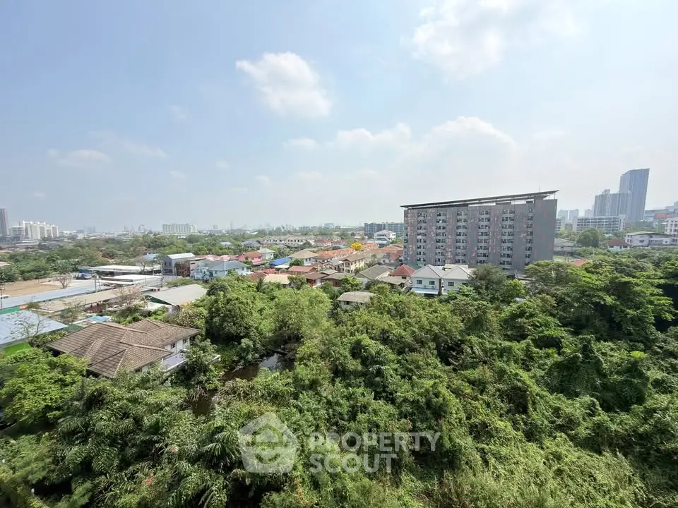Panoramic cityscape view with lush greenery and modern buildings under a clear blue sky.