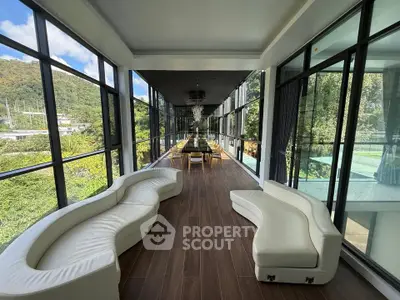 Luxurious modern living space with panoramic glass walls and elegant seating, offering stunning views of lush greenery.