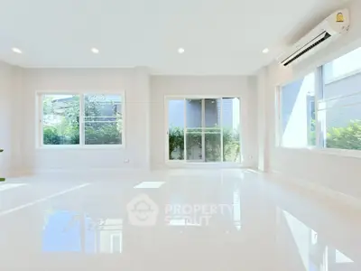 Spacious sunlit living room with large windows and modern air conditioning unit.