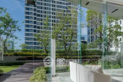Modern building view from glass-walled interior with lush garden and bright blue sky.