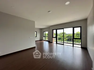 Spacious living room with large windows and balcony access, offering a serene green view.
