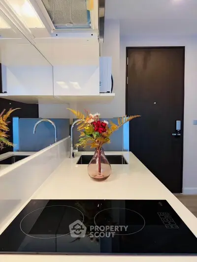 Modern kitchen with sleek induction cooktop and elegant floral centerpiece on white countertop.
