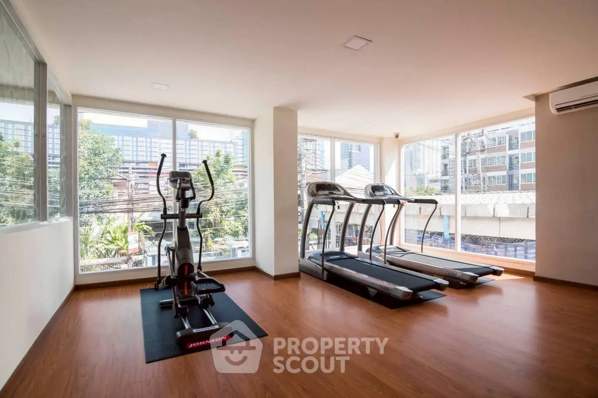 Spacious gym with modern equipment and large windows offering city views.