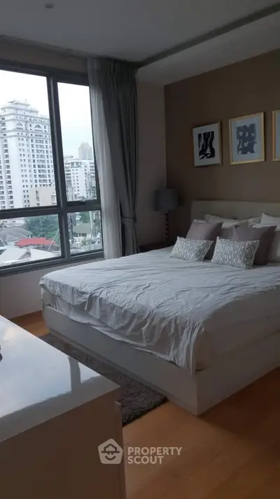 Modern bedroom with large window offering city view, stylish decor, and cozy ambiance.