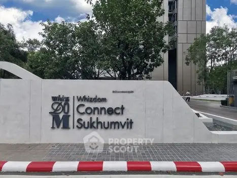 Modern building entrance with sleek signage at Whizdom Connect Sukhumvit, surrounded by lush greenery.