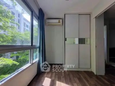 Bright room with large window and built-in wardrobe, featuring air conditioning and wooden flooring.