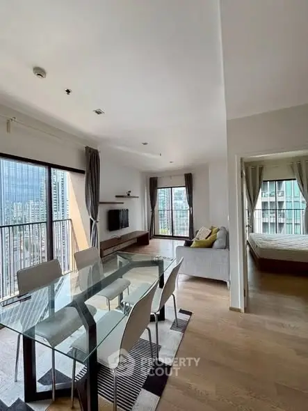 Modern open-plan living room with dining area and city view, featuring sleek furniture and large windows.