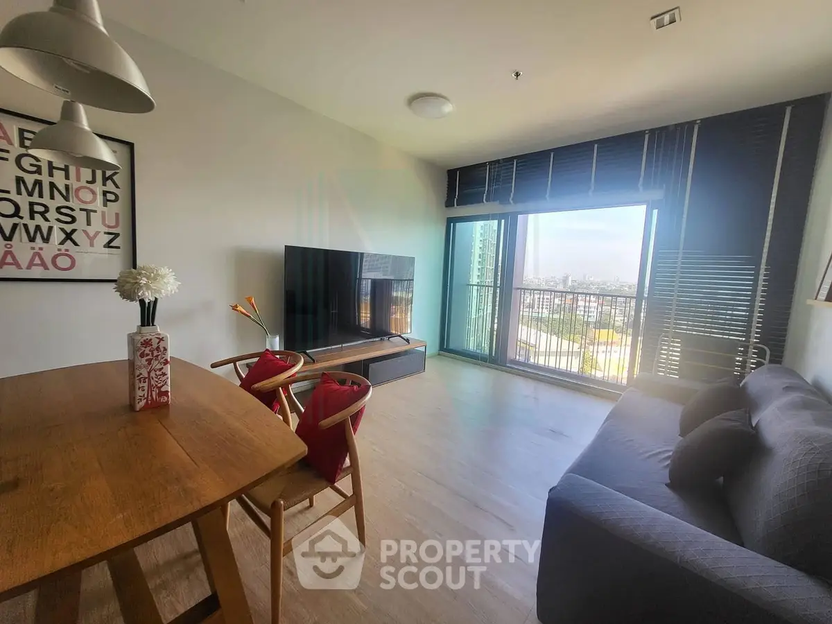 Modern living room with large TV, stylish furniture, and city view through large windows.