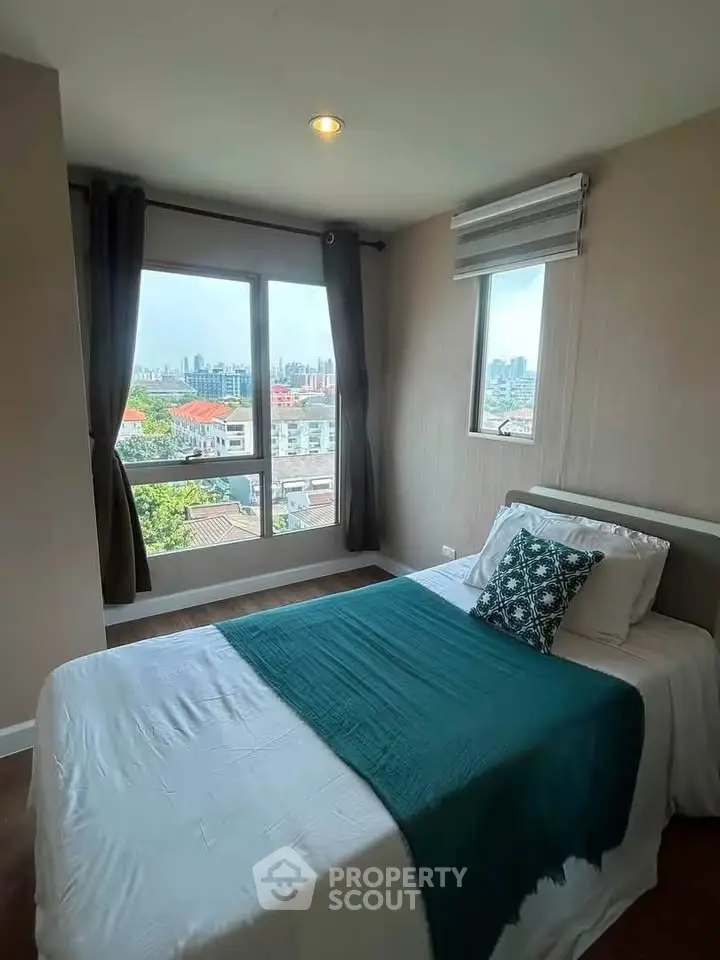 Cozy bedroom with city view, featuring a comfortable bed and large windows for natural light.
