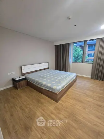 Spacious bedroom with wooden flooring and large window in modern apartment.