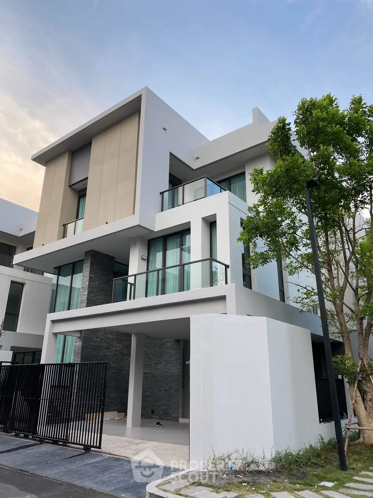 Modern three-story house with sleek design and large windows in a serene neighborhood.