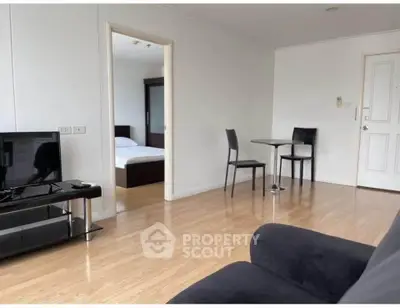Spacious living room with wooden flooring and modern furniture, leading to a cozy bedroom.