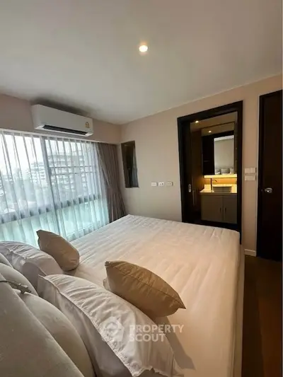 Modern bedroom with large window and ensuite bathroom in a stylish apartment.