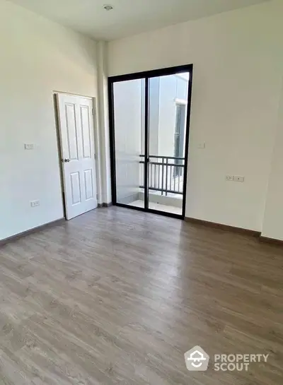 Spacious empty room with wooden flooring and large glass door leading to a balcony, ideal for customization.