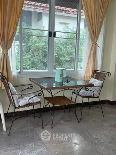 Charming breakfast nook with garden view, featuring elegant wrought iron chairs and a glass-top table.