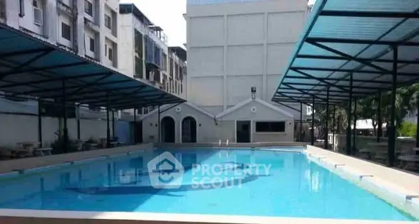 Spacious outdoor swimming pool with covered seating area in modern residential complex.
