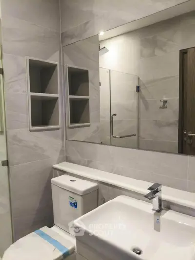 Modern bathroom with sleek fixtures and neutral tiles, featuring a spacious mirror and built-in shelving.