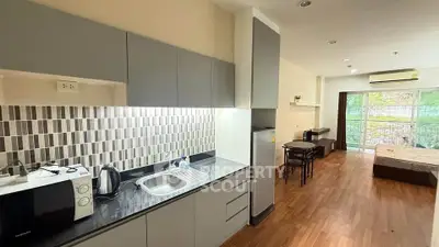 Modern studio apartment with sleek kitchen and cozy living area, featuring wood flooring and ample natural light.