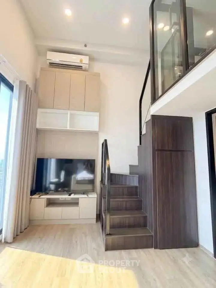 Modern loft apartment with stylish staircase and large TV, featuring high ceilings and natural light.