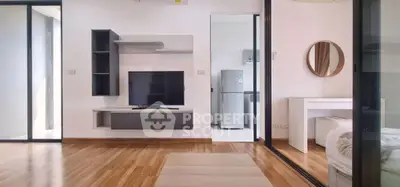 Modern living room with sleek TV unit and view into a minimalist bedroom and kitchen.
