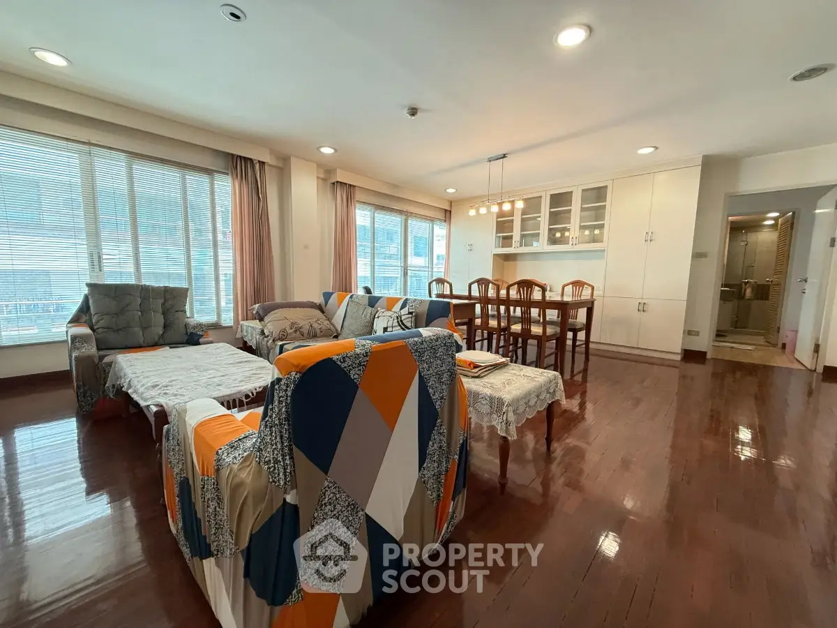 Spacious living room with modern furniture and dining area, featuring large windows and wooden flooring.
