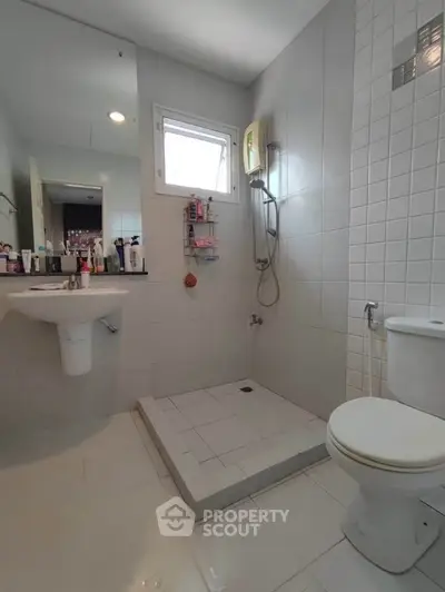 Modern bathroom with shower and white tiles, featuring a window for natural light.
