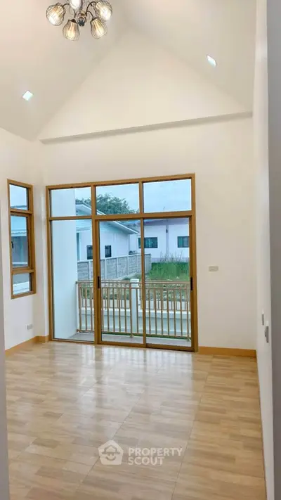 Spacious room with high ceiling and large windows overlooking a balcony in a modern home.