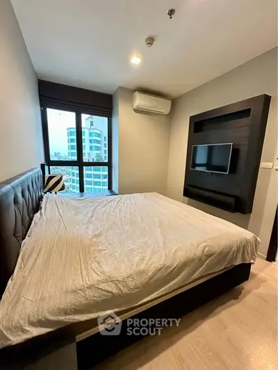Modern bedroom with large window and city view, featuring a wall-mounted TV and air conditioning.