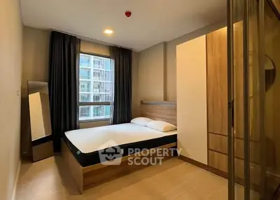 Modern bedroom with large window and wooden furniture in urban apartment.