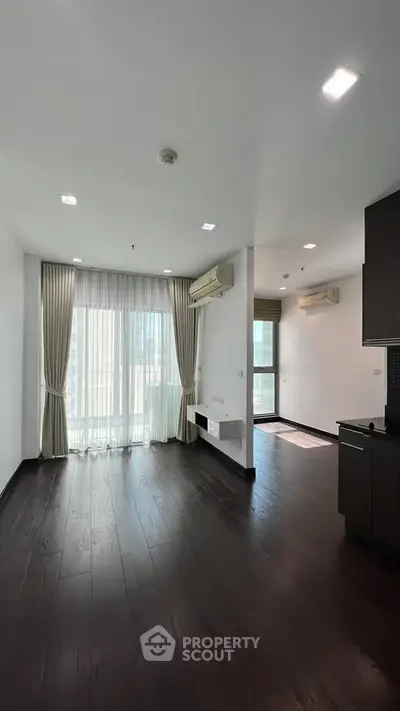 Spacious modern living room with dark wood flooring and large windows for natural light.