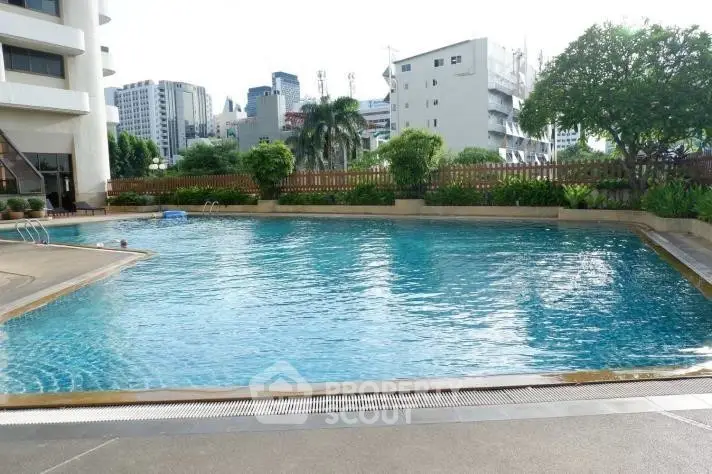 Spacious outdoor pool area with cityscape backdrop in modern residential complex.