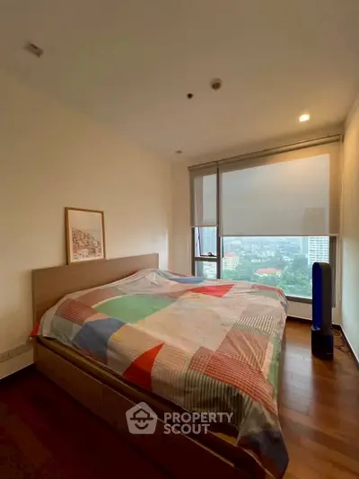 Spacious bedroom with large window offering stunning city views, featuring a cozy bed and elegant wooden flooring.