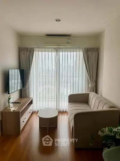 Cozy living room with large window, modern sofa, and wall-mounted TV, offering a bright and inviting atmosphere.