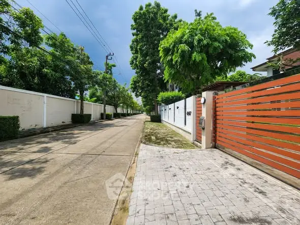 Charming residential street with lush greenery and modern gated entrance.