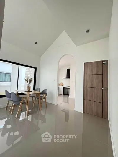 Modern dining area with high ceiling and archway leading to sleek kitchen.