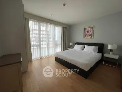 Spacious bedroom with large windows and elegant decor in modern apartment.