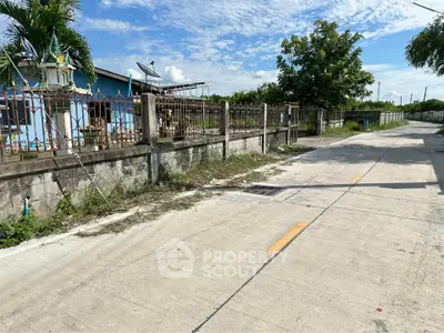 Charming suburban street view with a fenced property and lush greenery under a clear blue sky.