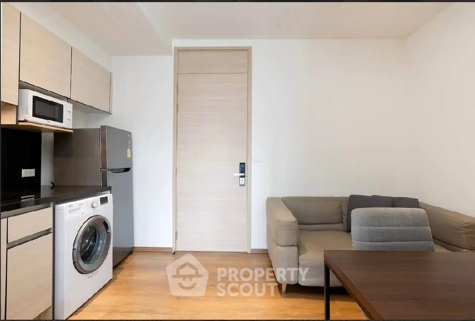 Modern living room with washing machine, fridge, and cozy sofa in a compact apartment.