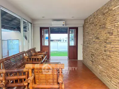 Charming sunlit room with rustic stone wall and bamboo furniture, perfect for relaxation.
