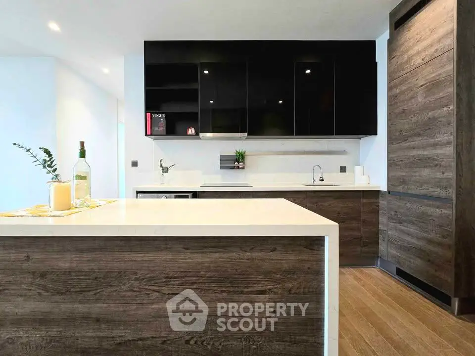 Modern kitchen with sleek black cabinets and wooden accents, featuring a spacious island and elegant lighting.