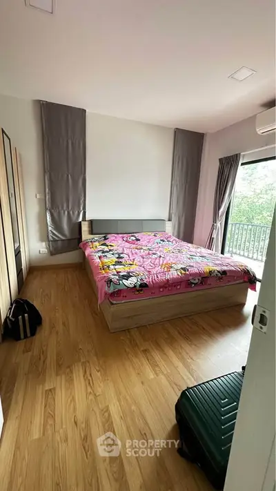 Cozy bedroom with wooden flooring and balcony view, featuring modern decor and ample natural light.