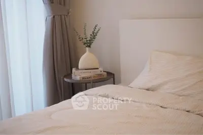 Cozy bedroom with elegant decor and natural light, featuring a stylish side table and soft bedding.