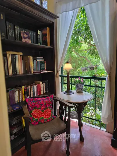Charming reading nook with garden view, featuring a cozy chair, elegant table, and bookshelf in a serene setting.