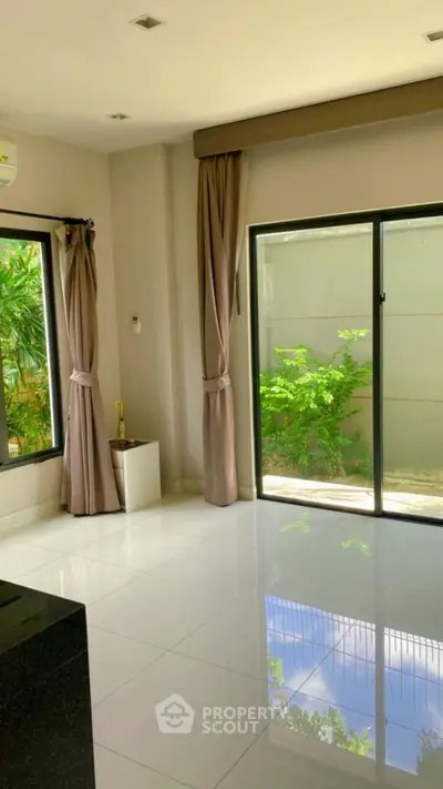 Bright living room with large windows and garden view, featuring elegant curtains and glossy white tiles.